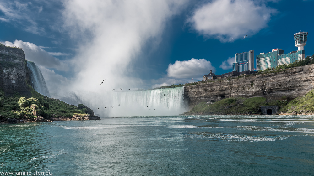Blick vom Fluss aus zu den kanadischen Fällen und zum Ort Niagara Falls (Ontario)