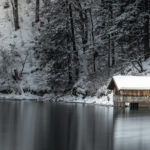 verschneites Bootshaus am winterlichen Alpsee