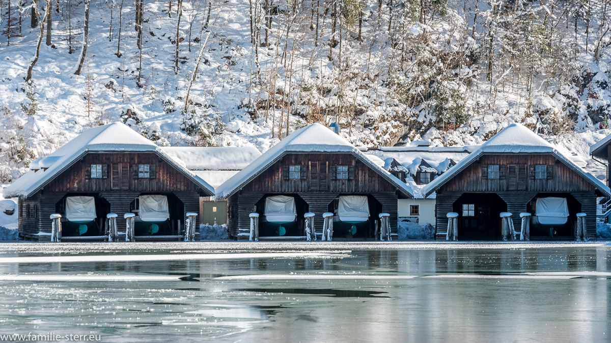 schneebedeckte Bootshäuser am vereisten Königssee