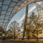 geschwungene Linien des Zeltdachs im Olympiapark über Bäumen mit herbstlich gefärbtem Laub