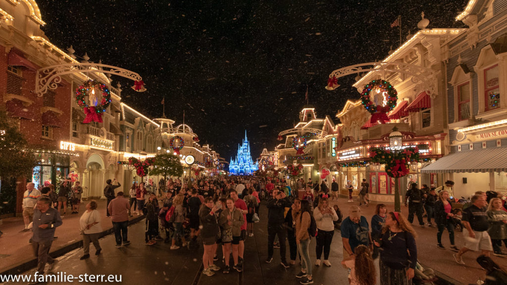 ein Blick über die nächtliche Main Street USA mit unglaublich vielen Menschen und künstlichem Schnee zum beleuchteten Schloss am Ende im Magic Kingdom Themenpark