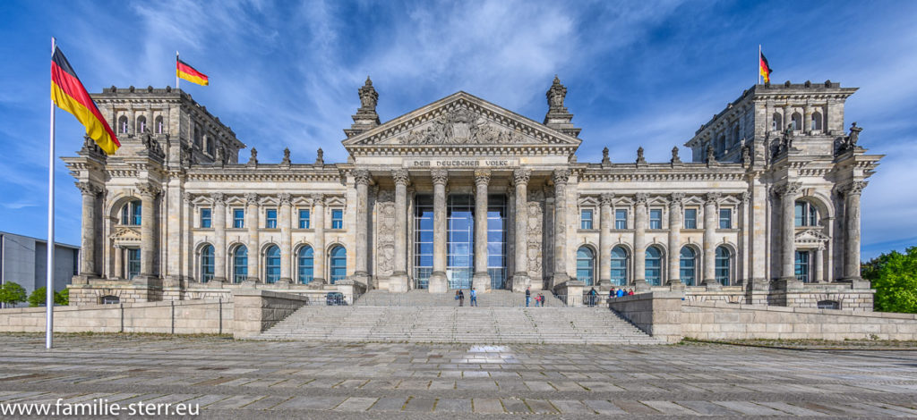 Vorderansicht des Berliners Reichstagsgebäudes mit wehender Deutschlandfahne bei leichter Bewölkung am blauen Himmel