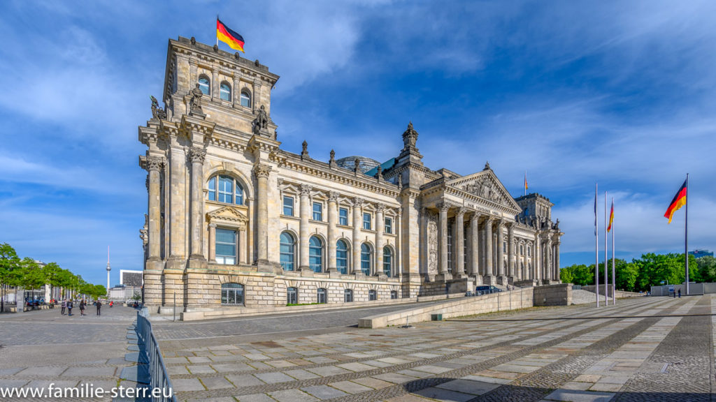 Seitliche Sicht aut das Berliners Reichstagsgebäude mit wehender Deutschlandfahne bei leichter Bewölkung am blauen Himmel