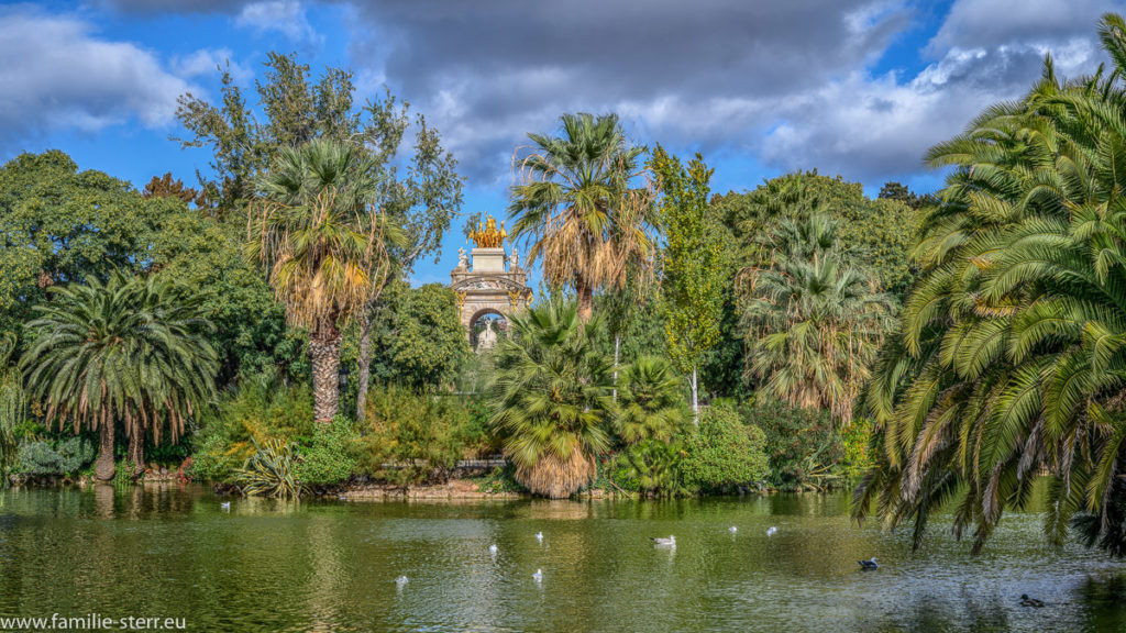 Blick über den See im Parc De La Ciutadella durch Palmen auf die Cascada Monumental Barcelona