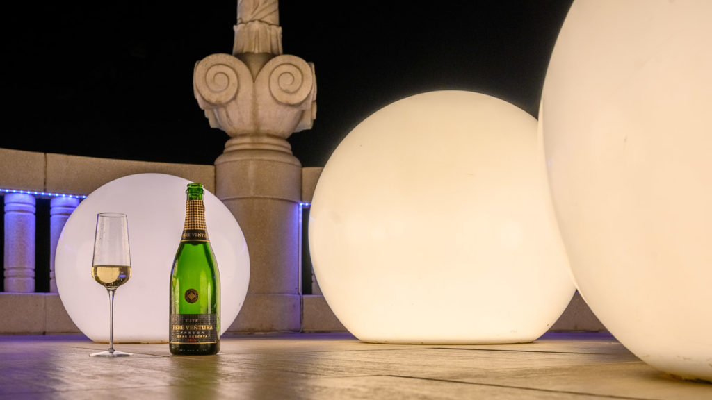 Flasche Cava Tresor und ein Glas Casa vor der beleuchteten Dekoration der Rooftop Bar im Hotel Casa Fuster in Barcelona