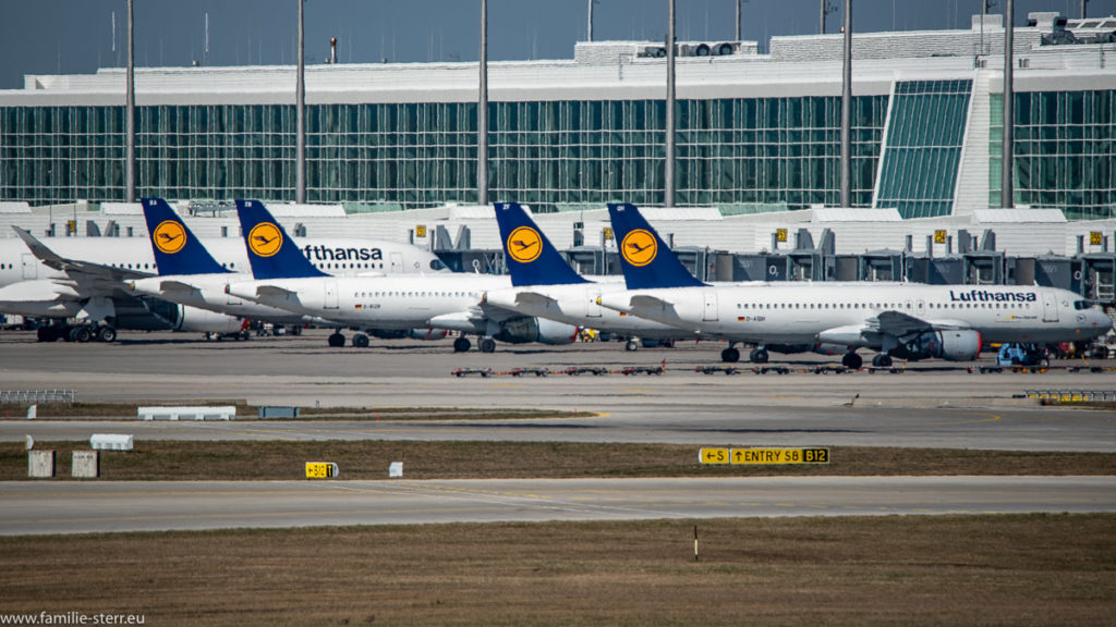 abgestellte Flugzeuge mit roten Triebwerksabdeckungen vor dem Satelliten des Terminals 2 am Flughafen München