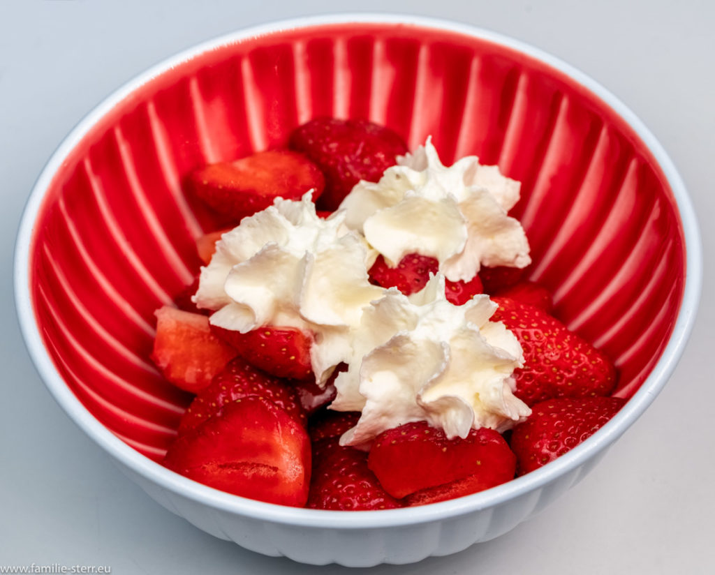 Erdbeeren mit 3 Sahnehäubchen in einer roten Schüssel