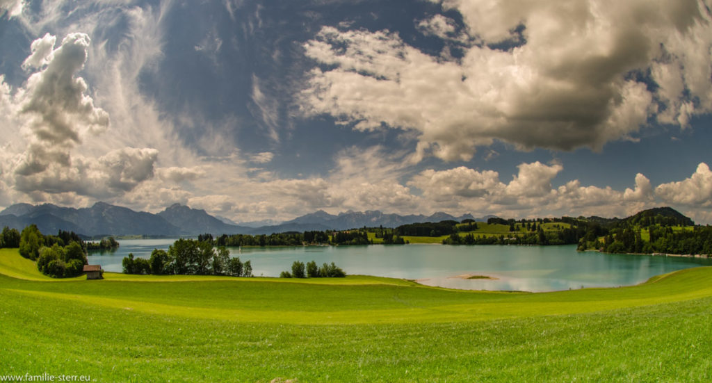 Blick über den Forggensee in die bayerischen Alpen mit weißen Kumuluswolken im weiß-blauen Himmel