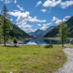 Blick vom nördlichen Ende des Neves - Stausees in Richtung Süden zur Staumauer bei strahlendem weiß-blauem Himmel