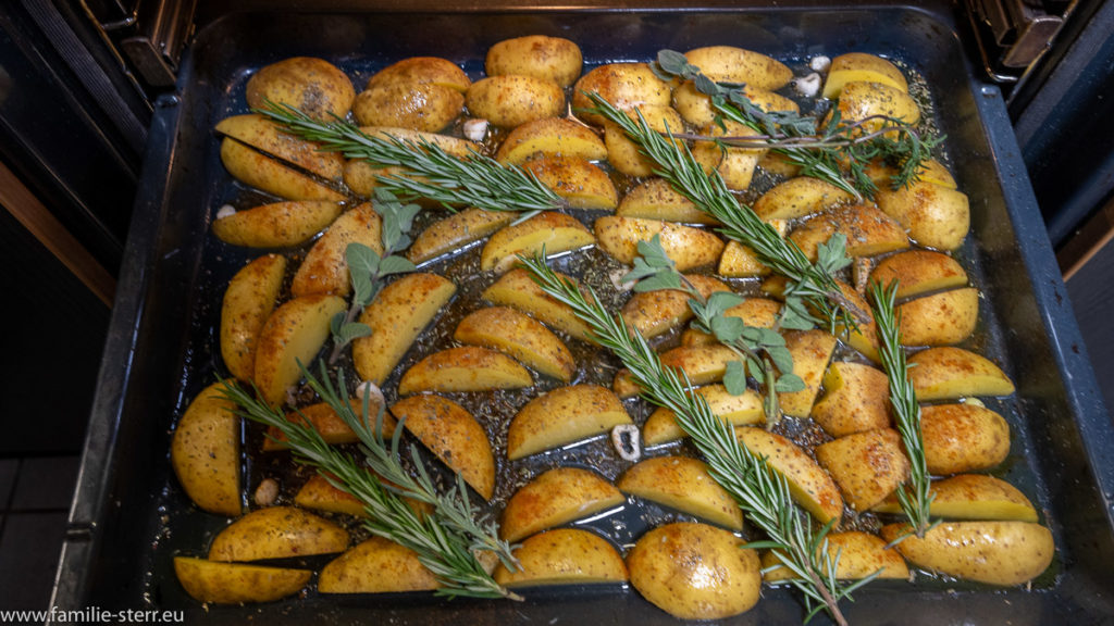 Kartoffelspalten bedeckt von vielen Kräutern und Rosmarin auf einem Backblech