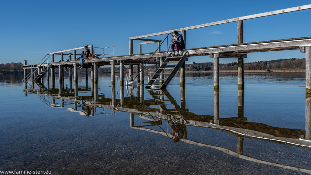 der Steg des Strandbads Breitbrunn am Chiemsee spiegelt sich im Wasser