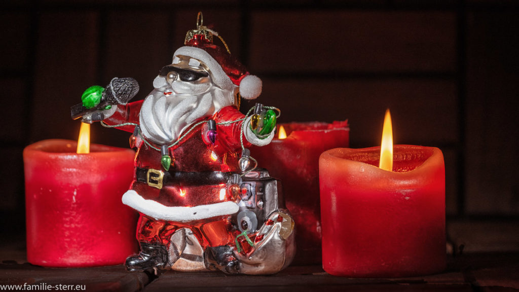 Christbaumfigur in Form eines singenden Weihnachtsmanns vor drei Adventskerzen