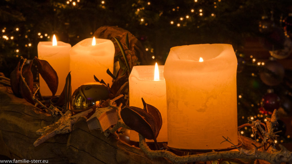 vier brennende Kerzen auf einem Weihnachtsgesteck