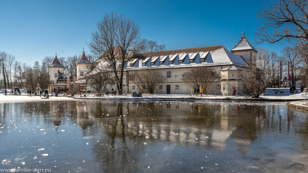 das Schloss Blutenburg spiegelt sich im Eis des zugefrorenen Schlossteichs an einem eiskalten Wintertag