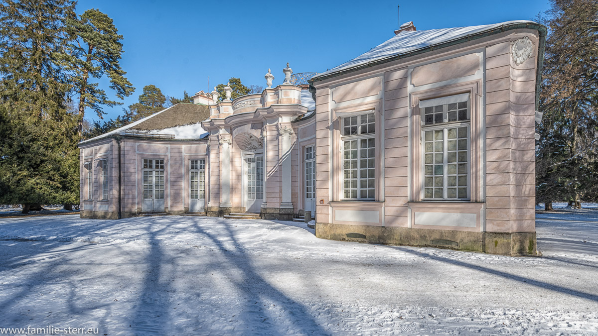 das Jagdschloss Amalienburg im winterlichen Schlosspark unter strahlend blauem Himmel