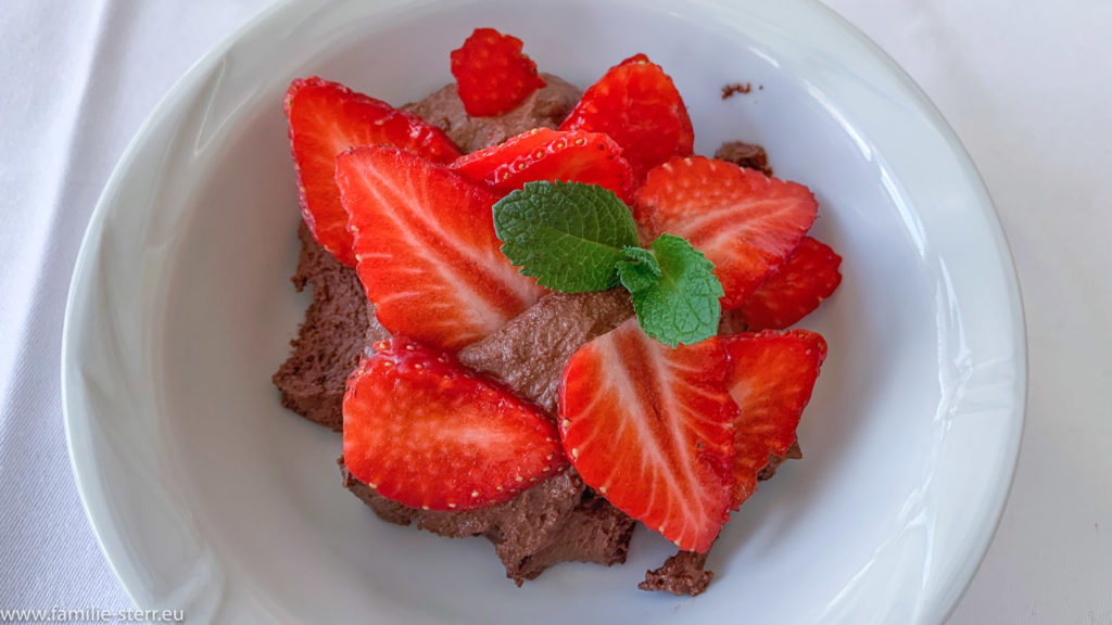 Mousse au Chocolat in einer weißen Schale, verziert mit Erbeerscheiben und zwei Minzblättern