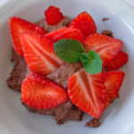 Mousse au Chocolat in einer weißen Schale, verziert mit Erbeerscheiben und zwei Minzblättern