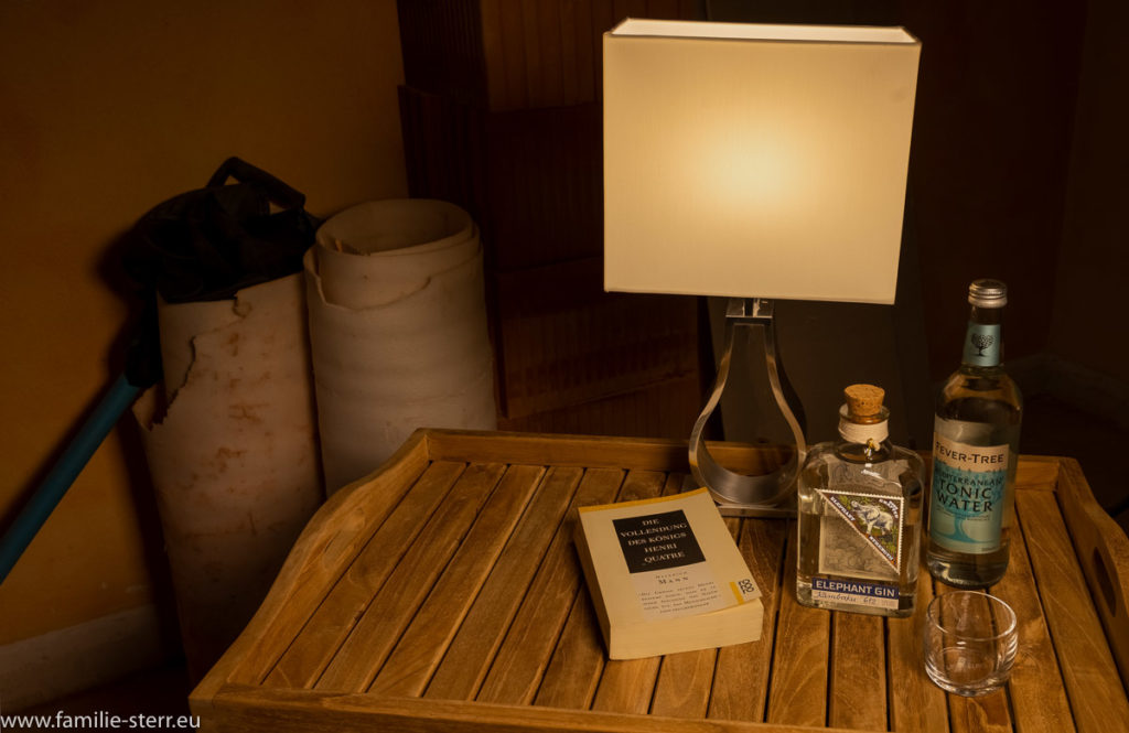 kleine Lampe, Gin, Tonicwasser, ein Glas und ein Buch auf einem Teakholztablett vor Baumaterial auf der Baustelle