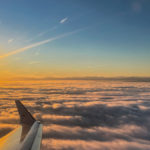 Sonnenaufgang über einer einer geschlossenen Wolkendecke mit den Alpen im Hintergrund, aufgenommen aus einem Flugzeug