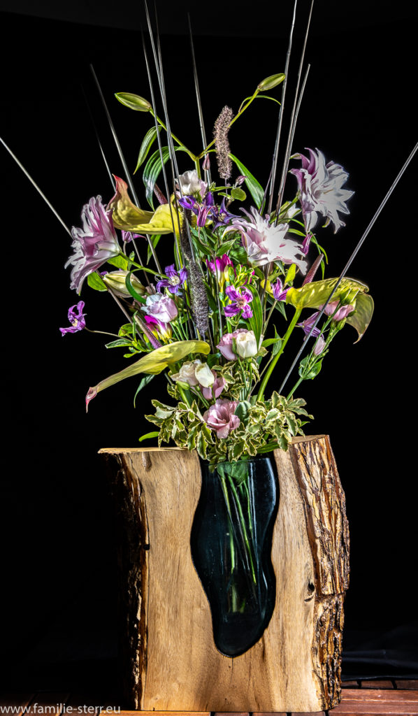 festliches Blumengesteck in rosa Farbtönen in einer Vase aus Glas und Holz