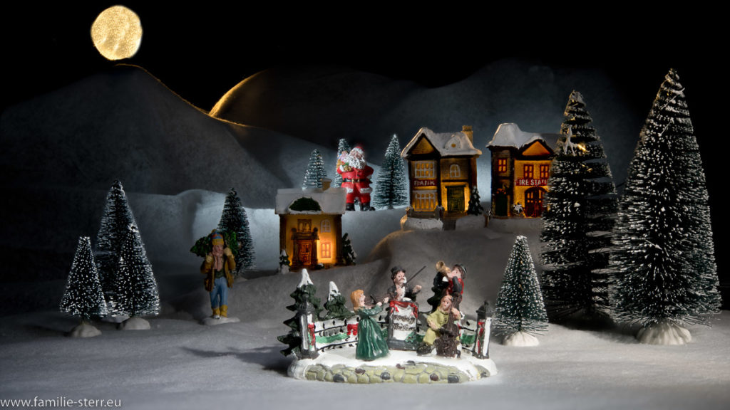 Szene aus unserem Weihnachtsdorf / der Chor singt Weihnachtslieder vor den Häusern