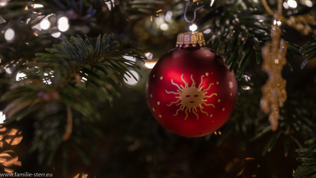 eine rote Christbaumkugel mit eine goldenen Sonne an unserem Weihnachtsbaum