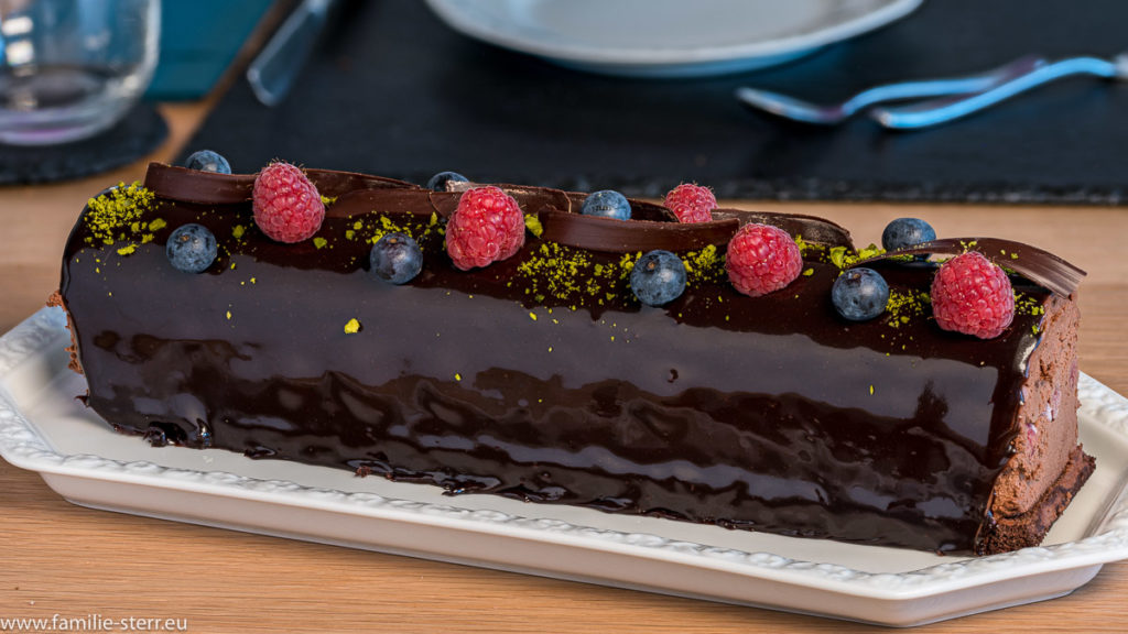 Astrids Schokotorte in "Baumform" nach Art der Sachertorte, dekoriert mit Schokospänen, Himbeere, Blaubeeren und Pistazien auf einer glänzenden Schikoladenglasur