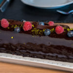 Astrids Schokotorte in "Baumform" nach Art der Sachertorte, dekoriert mit Schokospänen, Himbeere, Blaubeeren und Pistazien auf einer glänzenden Schikoladenglasur