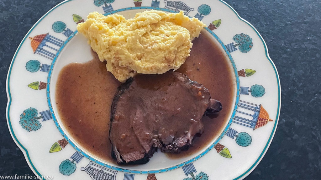 eine Scheibe geschmorte Wildschweinschulter mit Soße und Polenta auf einem weißen Teller / Brasato von der Wildscheinschulter