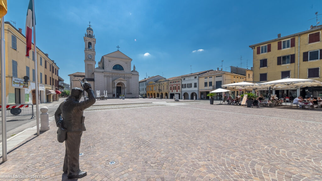 Statue von Peppone schaut über den Dorfplatz von Brescello auf die Kirche von Don Camillo