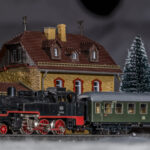 eine kleine Dampflok mit einem historischen Personenwagen steht im winterlichen Bahnhof - Märklin H0