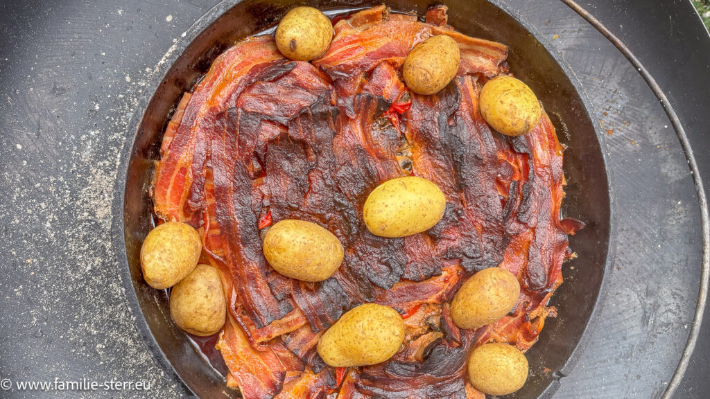 fertiges Schichtfleisch im Dutch Oven in einem Mantel aus knusprigem Bacon und ein paar mitgekochenten Kartoffeln