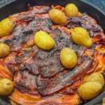 fertiges Schichtfleisch im Dutch Oven in einem Mantel aus knusprigem Bacon und ein paar mitgekochenten Kartoffeln