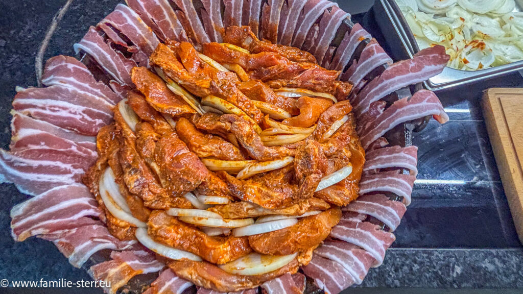der Dutch Oven wird mit den Steaks und den Zwiebeln in Schichten gefüllt