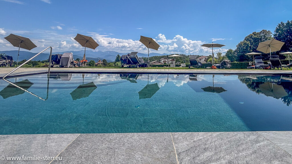 Blick in den Pool und über die Sonnenschirme im Garten des Hotels Solea Dolomiti mit Blick über das Etschtal in die Dolomiten