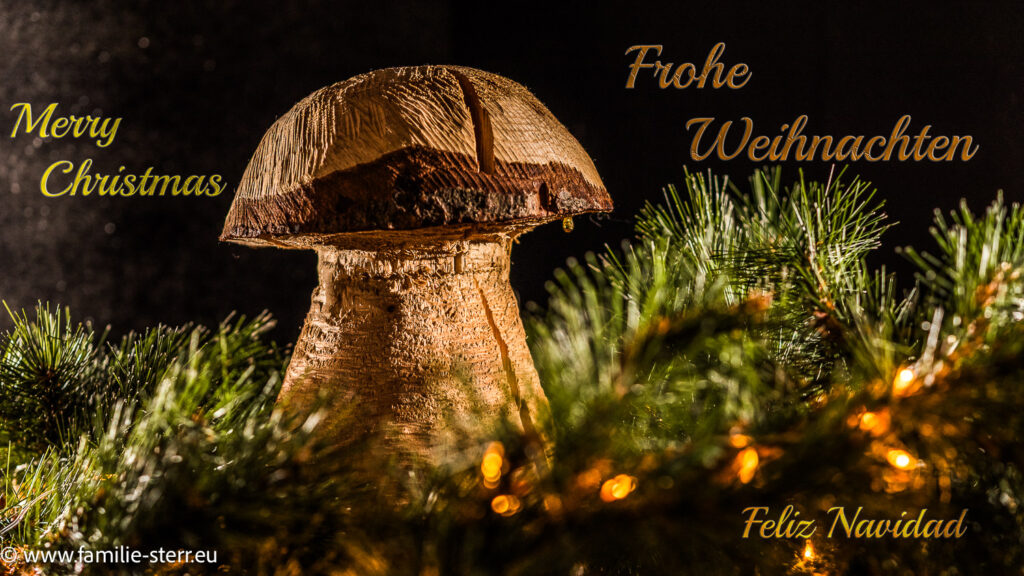 ein Pilz aus Holz geschniitzt zwischen Tannenzweigen und dem Schriftzug "Frohe Weihnachten"