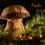 ein Pilz aus Holz geschniitzt zwischen Tannenzweigen und dem Schriftzug "Frohe Weihnachten"