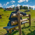 Thomas sitzt auf einer Bank auf einer Alm an der Rotwand bei Sexten in Südtirol und genießt das warme Wetter